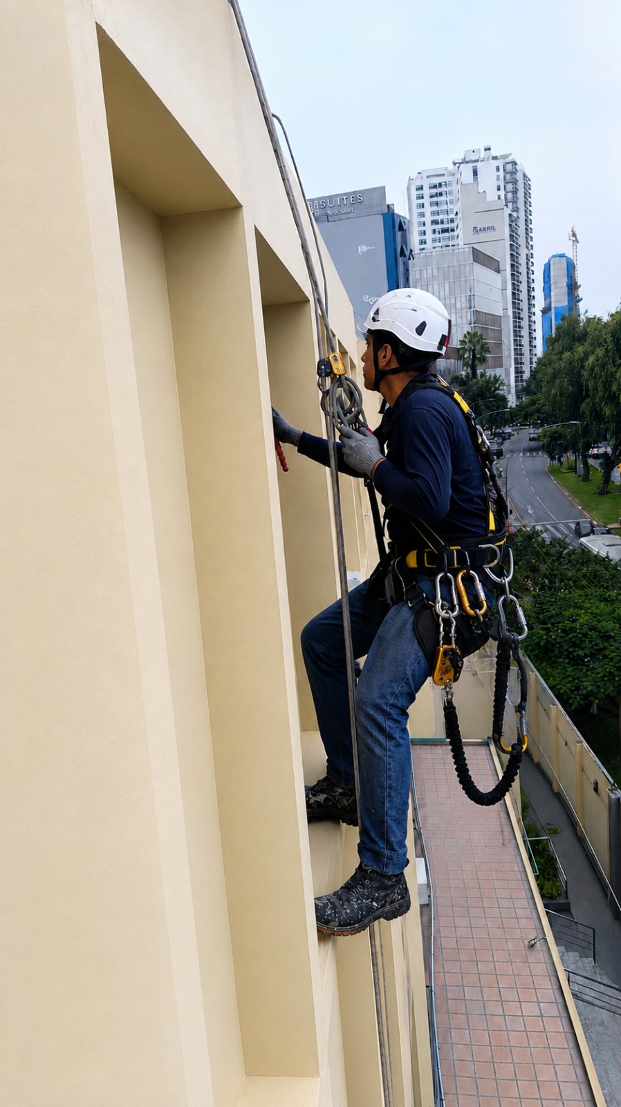 Técnico con arnés y casco descendiendo por cuerdas para pintar una fachada